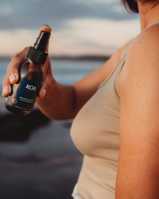 Woman spraying Magnesium Oil onto her upper arm with beach background.