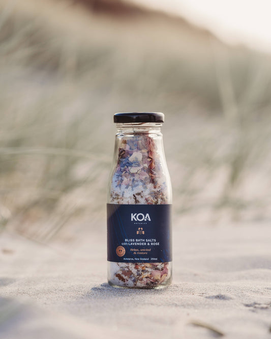Koa Bliss Bath Salts with Lavender & Rose sitting on the sand with the grasses behind.