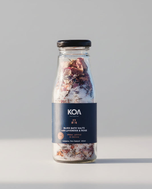 Koa Bliss Bath Salts with Lavender & Rose sitting on the sand with the ocean behind.
