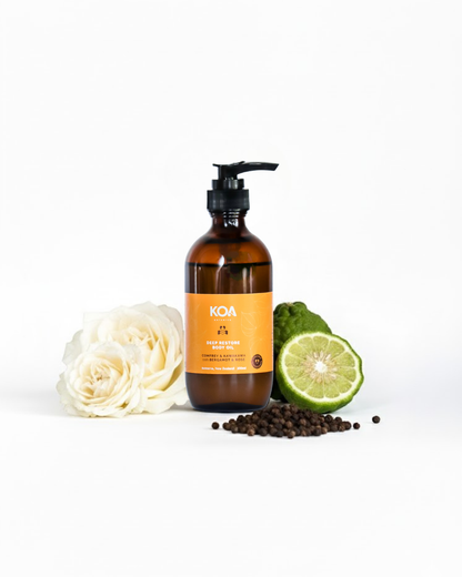 Brown KOA bottle with pump, lime, rose, and peppercorns on a white background