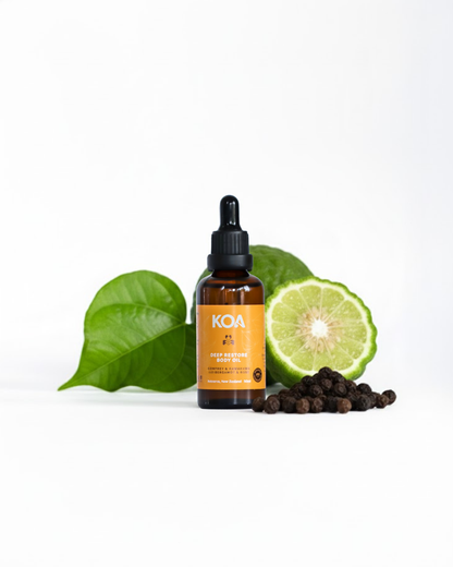 Bottle of KOA oil with lime, leaves, and peppercorns on a white background
