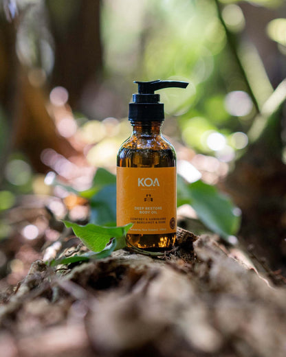 Bottle of KOA Restore oil on a forest floor with blurred greenery in the background