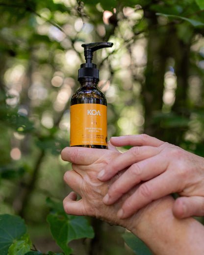 Hand holding a bottle labeled KOA against a blurred natural background