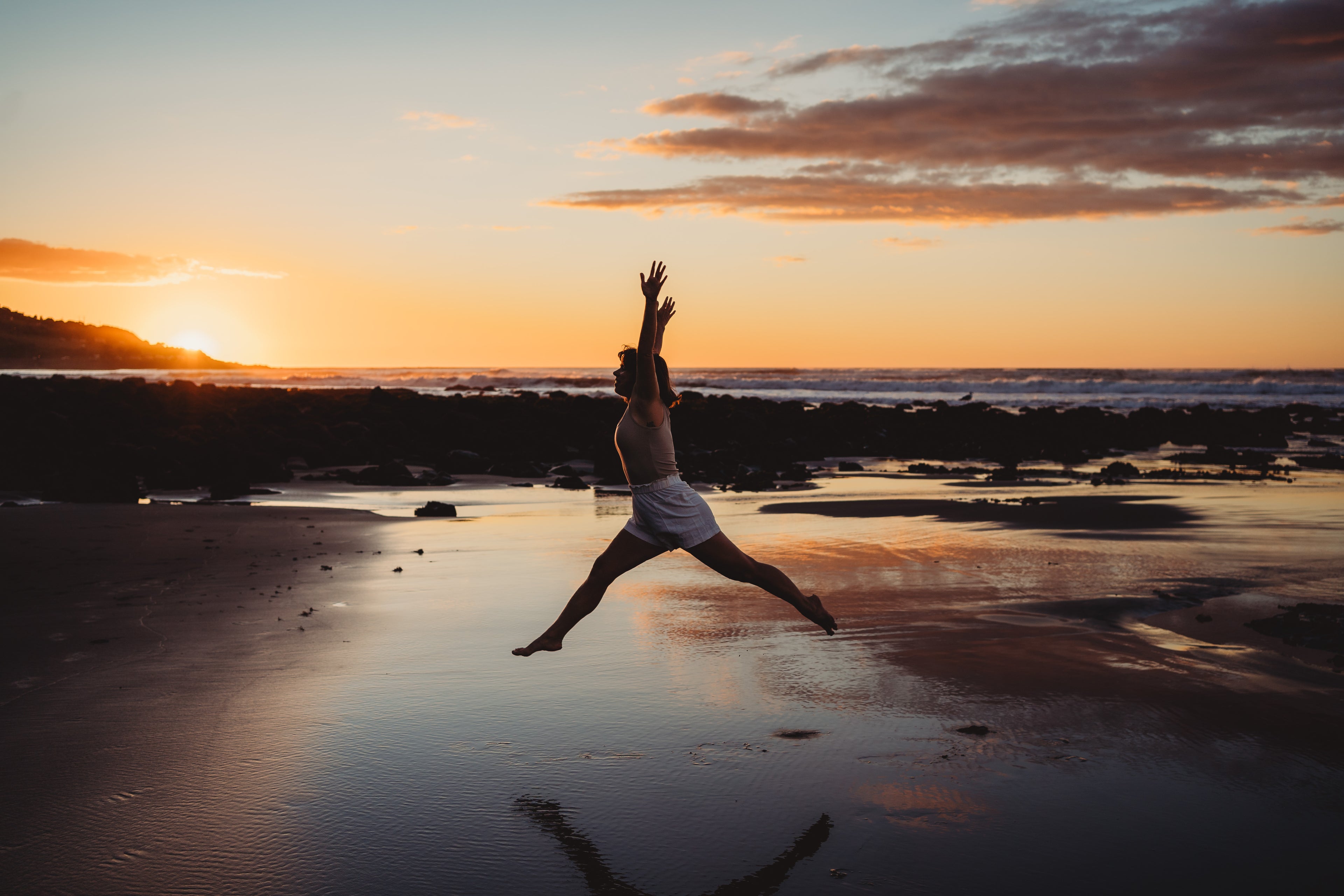 Woman joyfully leaping on beach at sunset