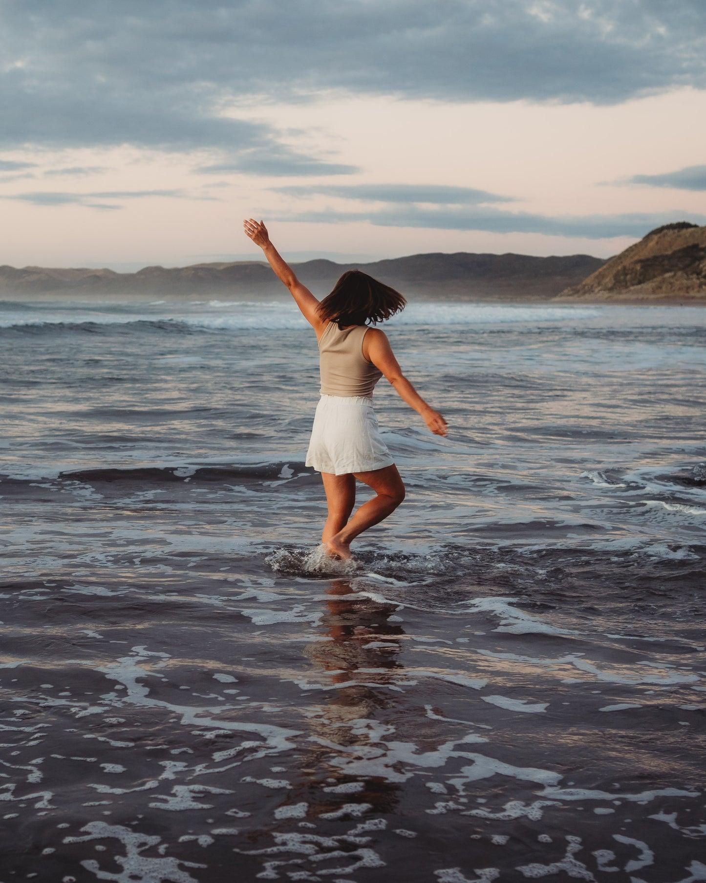 Woman walking through water at the shoreline with an ocean background. Taken from behind.