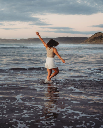 Woman walking through water at the shoreline with an ocean background. Taken from behind.