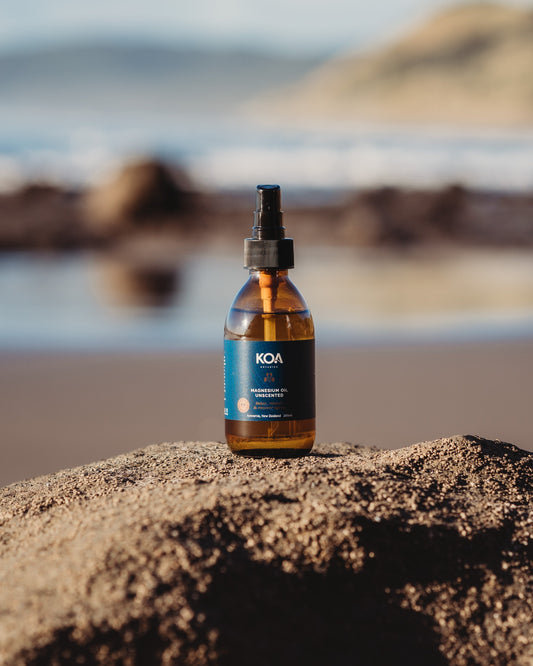 Magnesium Unscented Oil sitting on a rock with beach background.