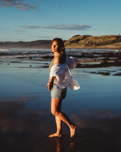 Female walking on the beach with arms outspread looking at the camera with ocean background.
