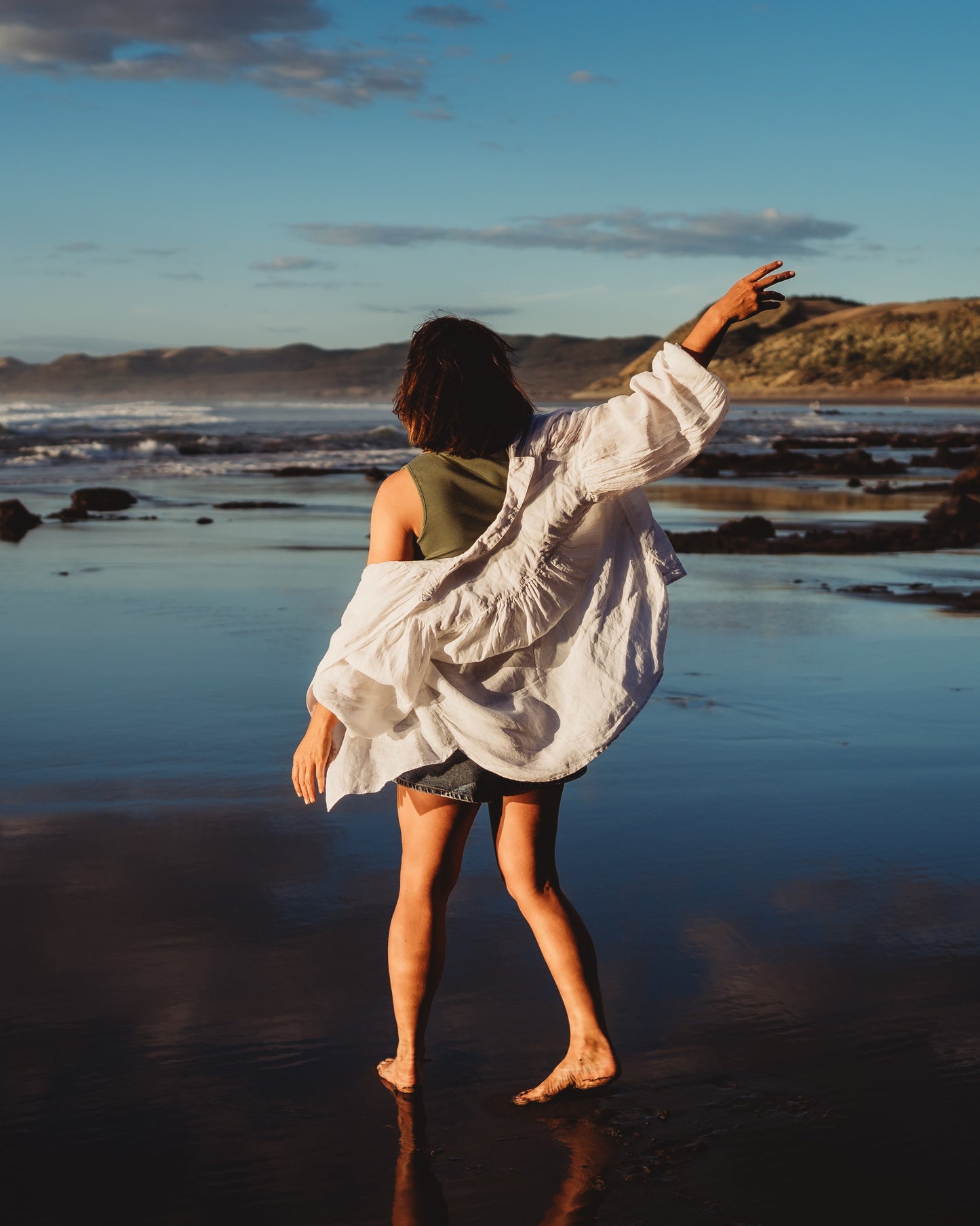 Woman walking along the shoreline with an ocean background. Taken from behind.