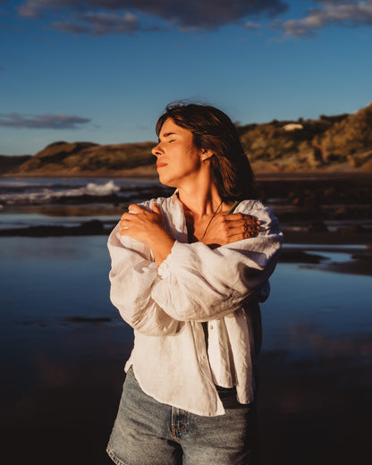 Woman hugging herself facing out to the ocean with closed eyes and a beach background.