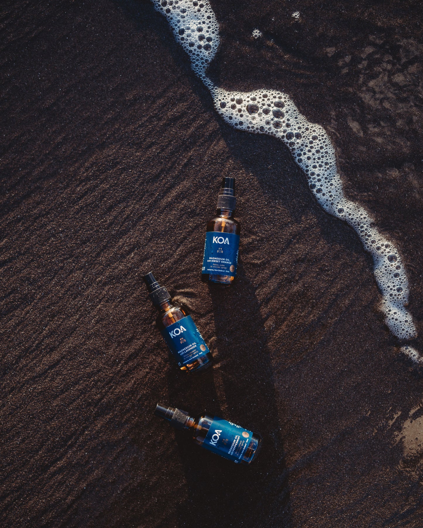 Three Magnesium Oils laying in the sand about to be washed over by a wave, taken from above.