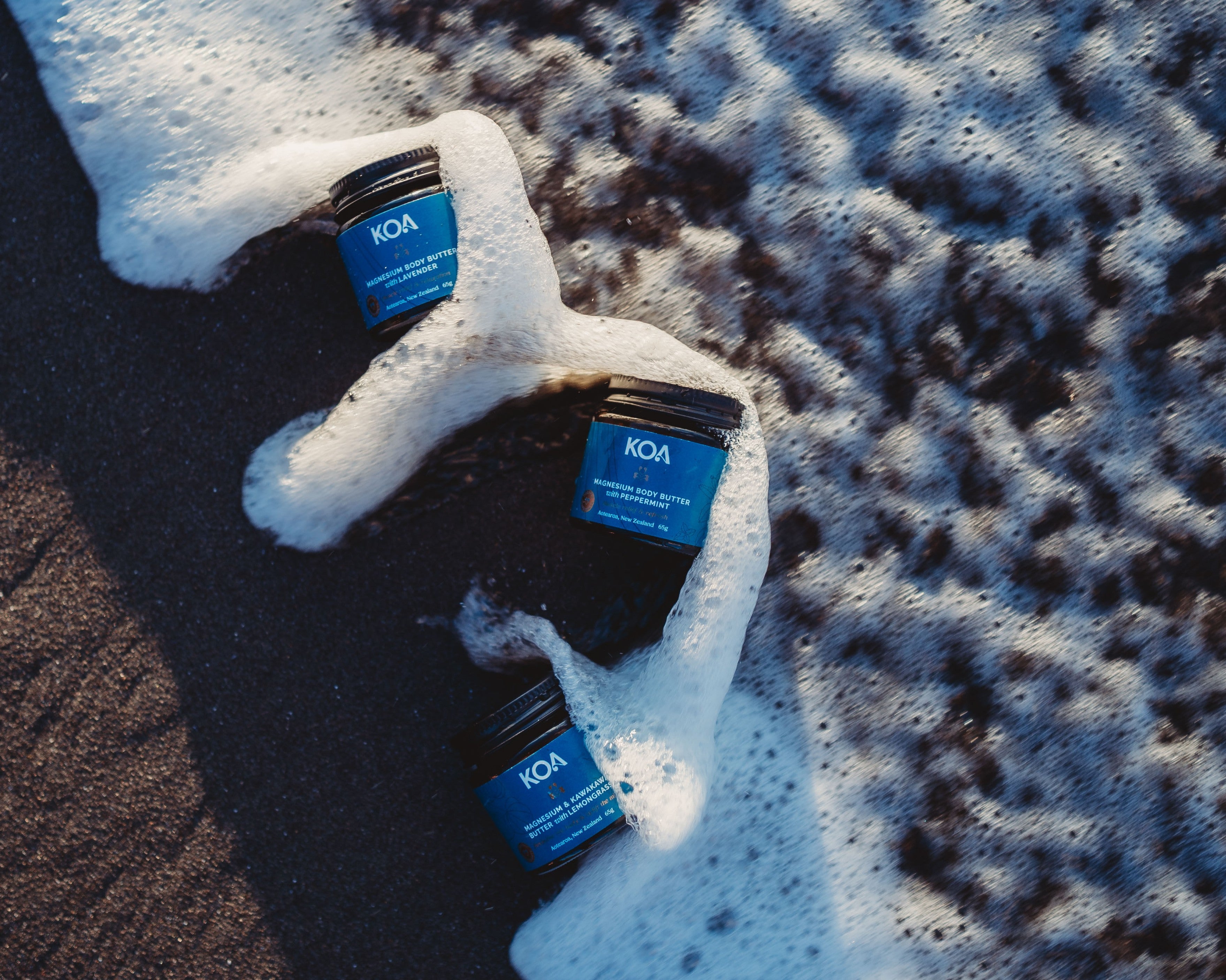 Jars of Koa Magnesium Butter in the sand and wave foam