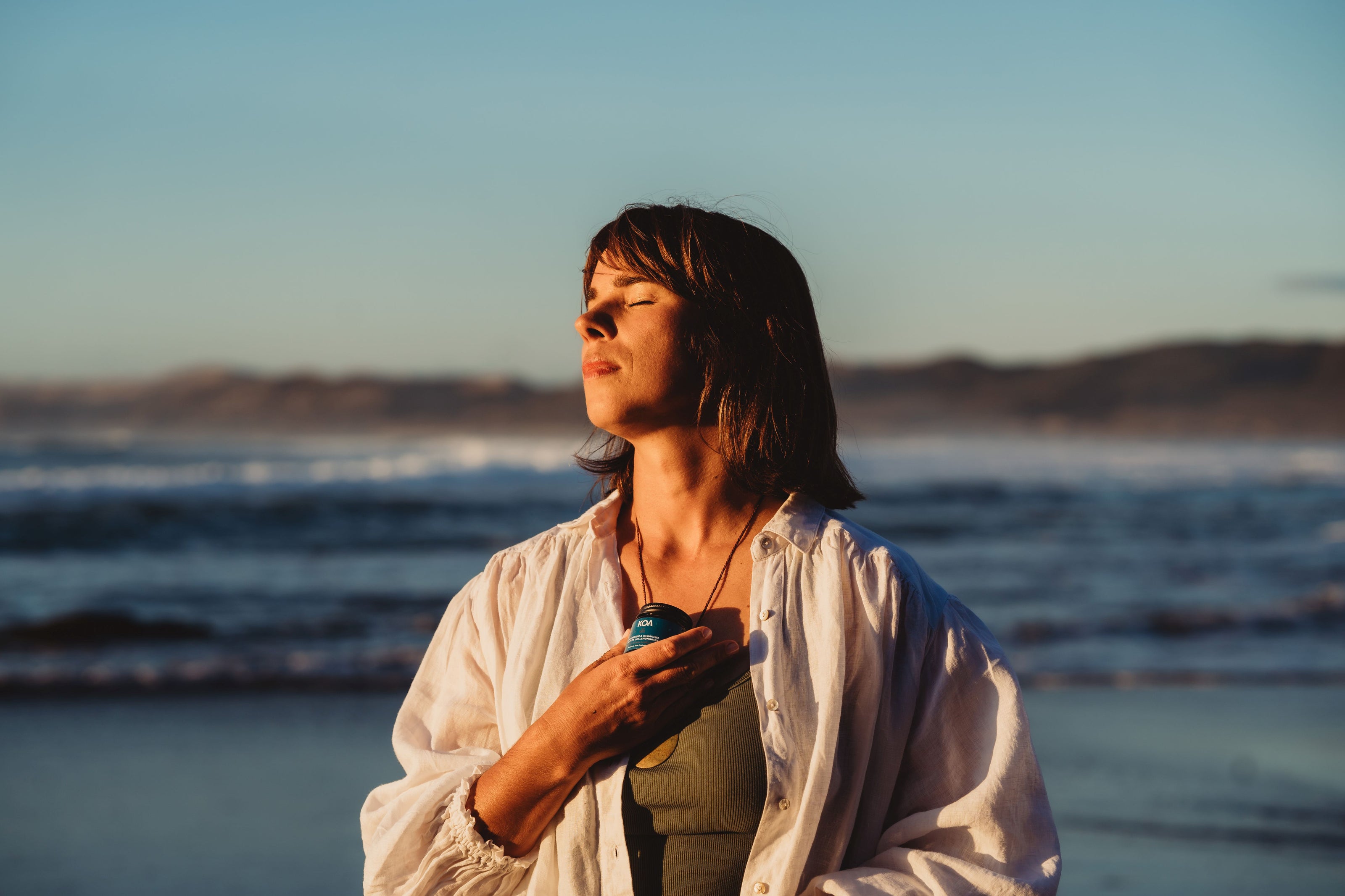 Woman at beach sunset looking calm holding KOA Magnesium Cream