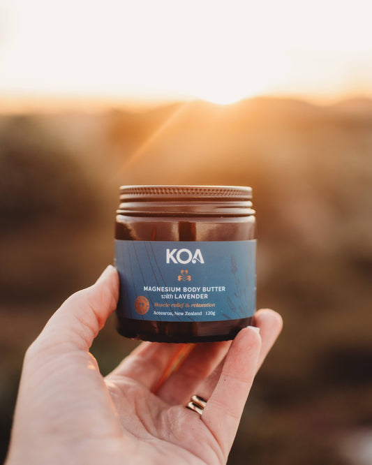 Koa Magnesium Body Butter with Lavender being held in a hand with sunset scenery behind.