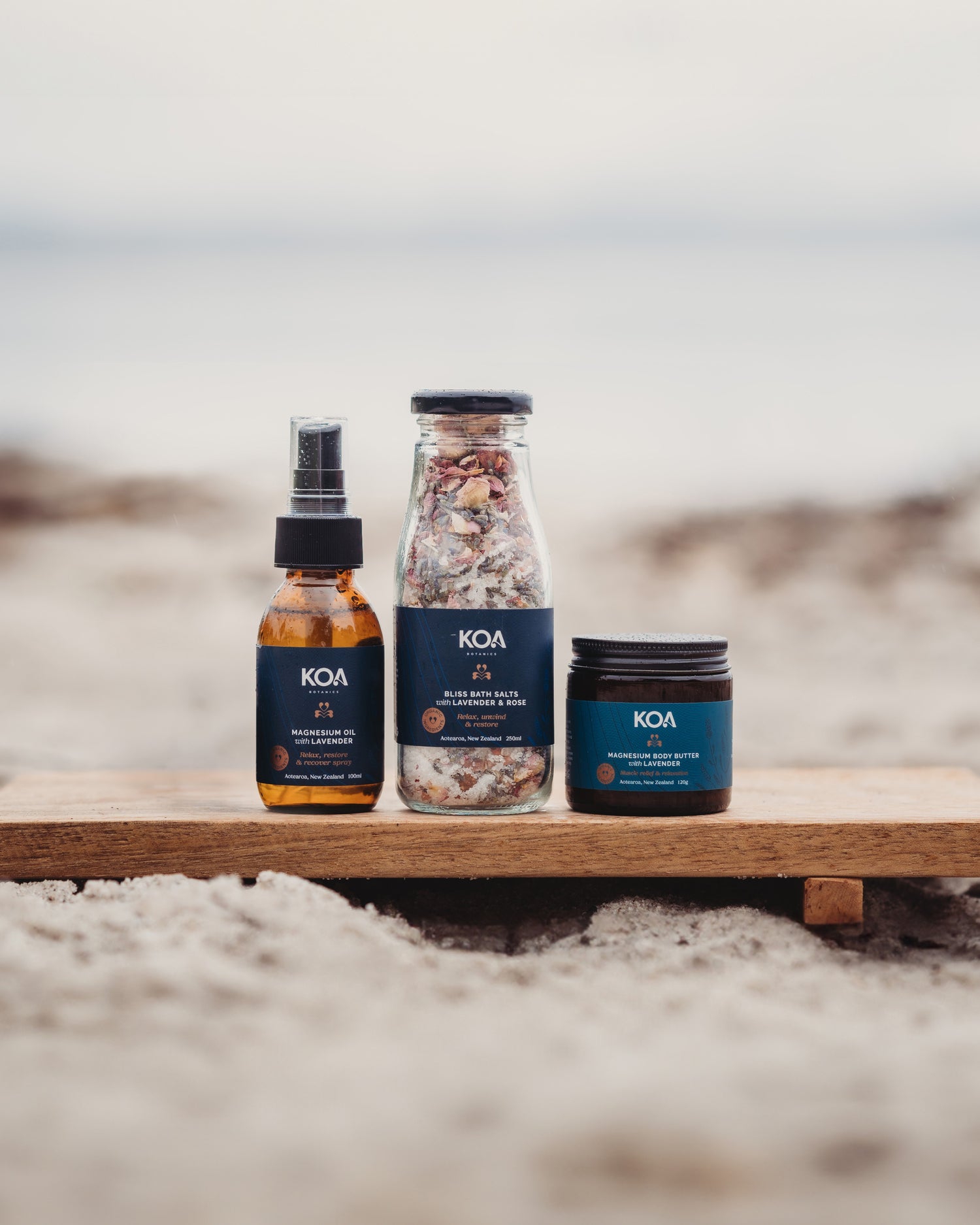 KOA skincare products on a wooden board with a beach background