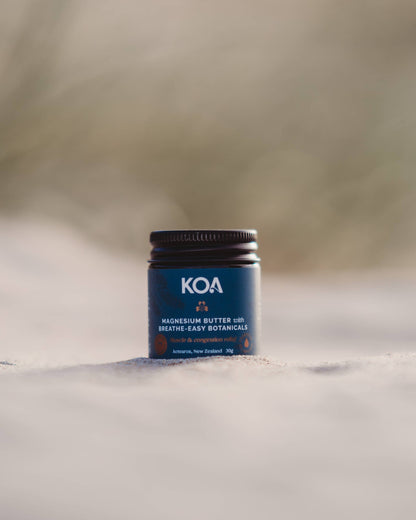 Magnesium Butter with Breathe Easy Botanicals sitting on the sand with grasses behind.