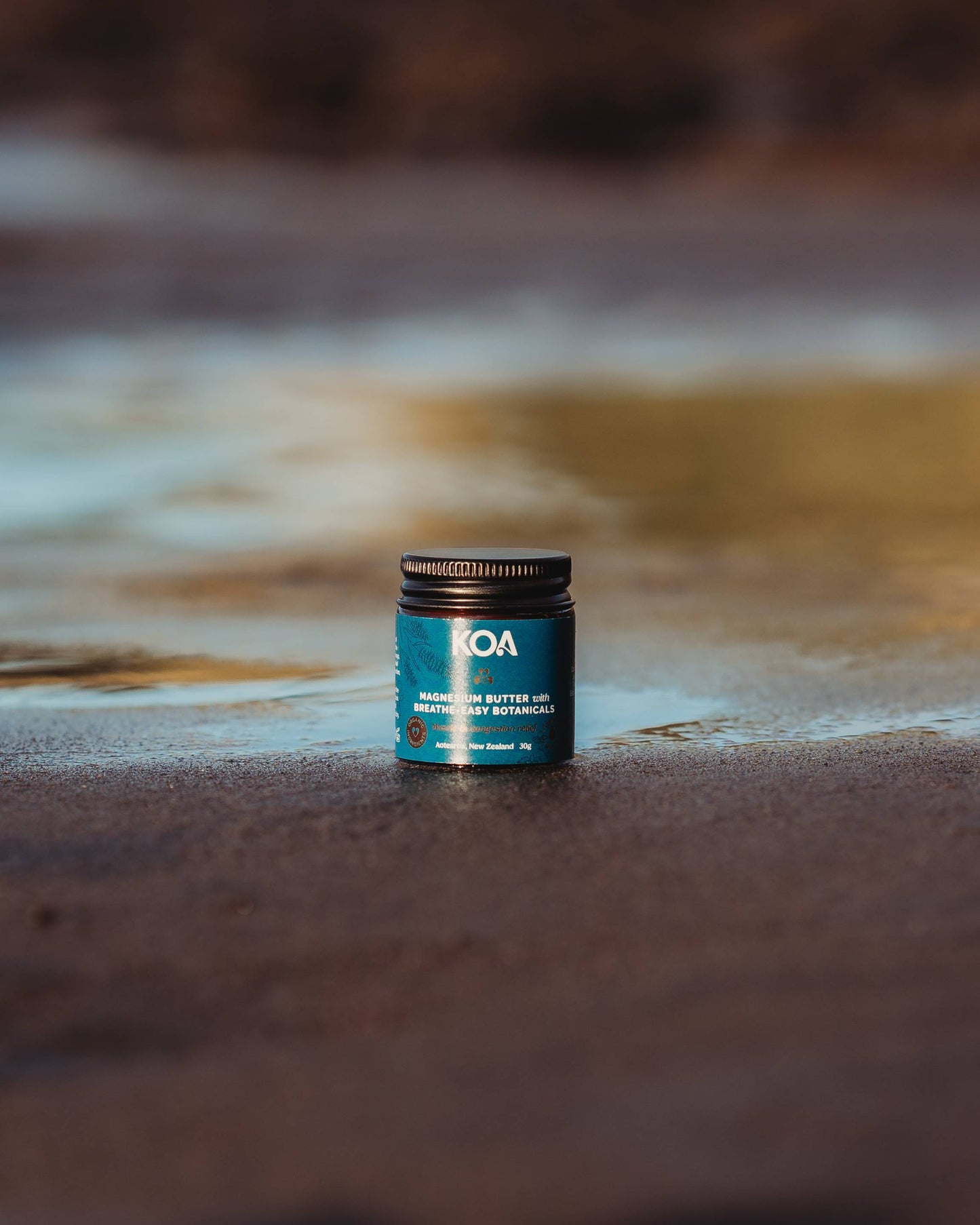 Magnesium Butter with Breathe Easy Botanicals sitting on the sand with beach background.