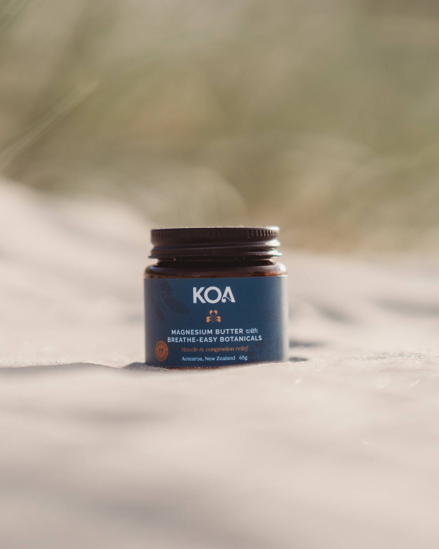 Magnesium Butter with Breathe Easy Botanicals sitting on the sand with grasses behind.