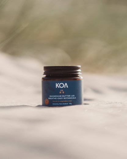 Magnesium Butter with Breathe Easy Botanicals sitting on the sand with grasses behind.
