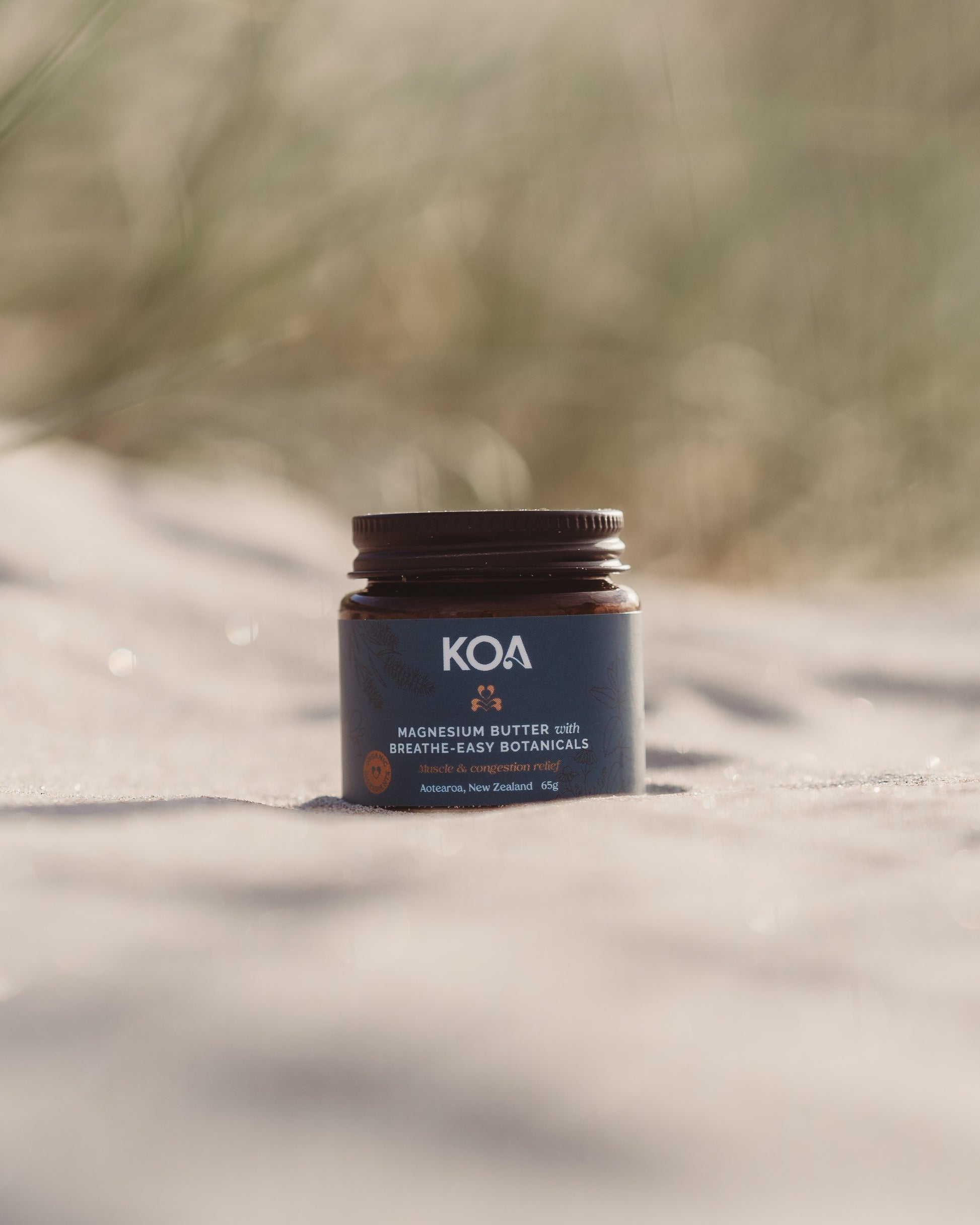 Magnesium Butter with Breathe Easy Botanicals sitting on the sand with grasses behind.