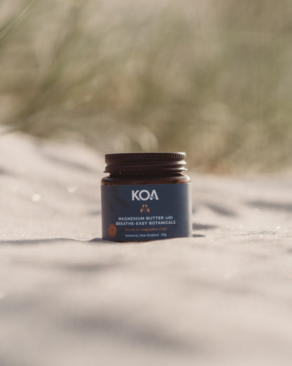 Magnesium Butter with Breathe Easy Botanicals sitting on the sand with grasses behind.