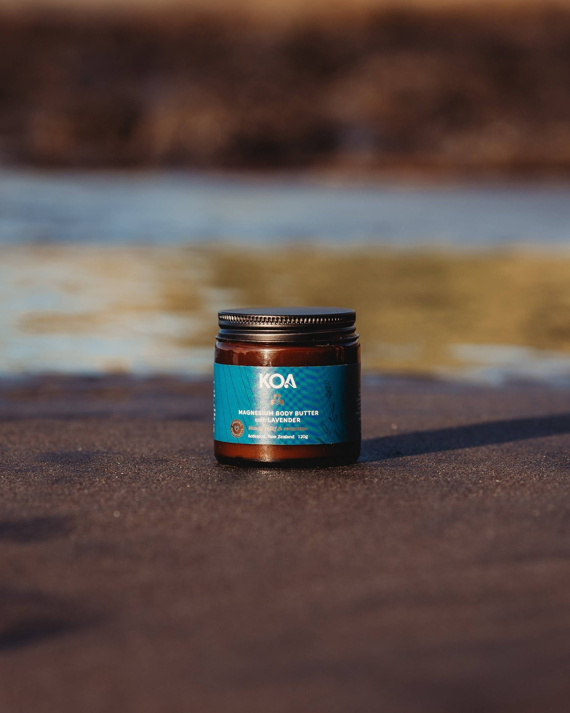Magnesium Butter with Lavender sitting on the sand with ocean behind.