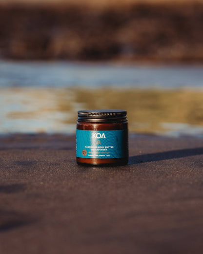 Magnesium Butter with Lavender sitting on the sand with ocean behind.