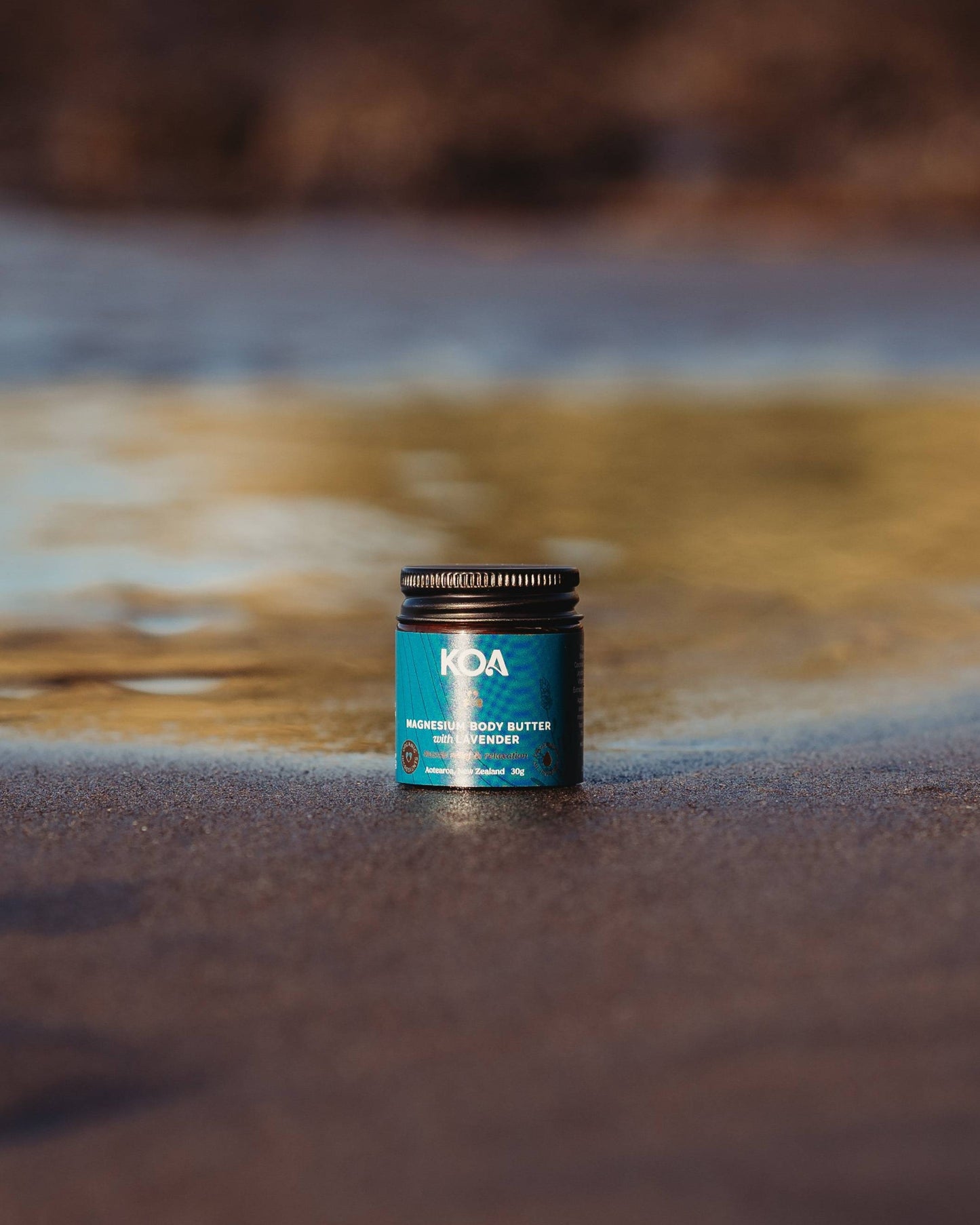 Magnesium Butter with Lavender sitting on the sand with an ocean background.