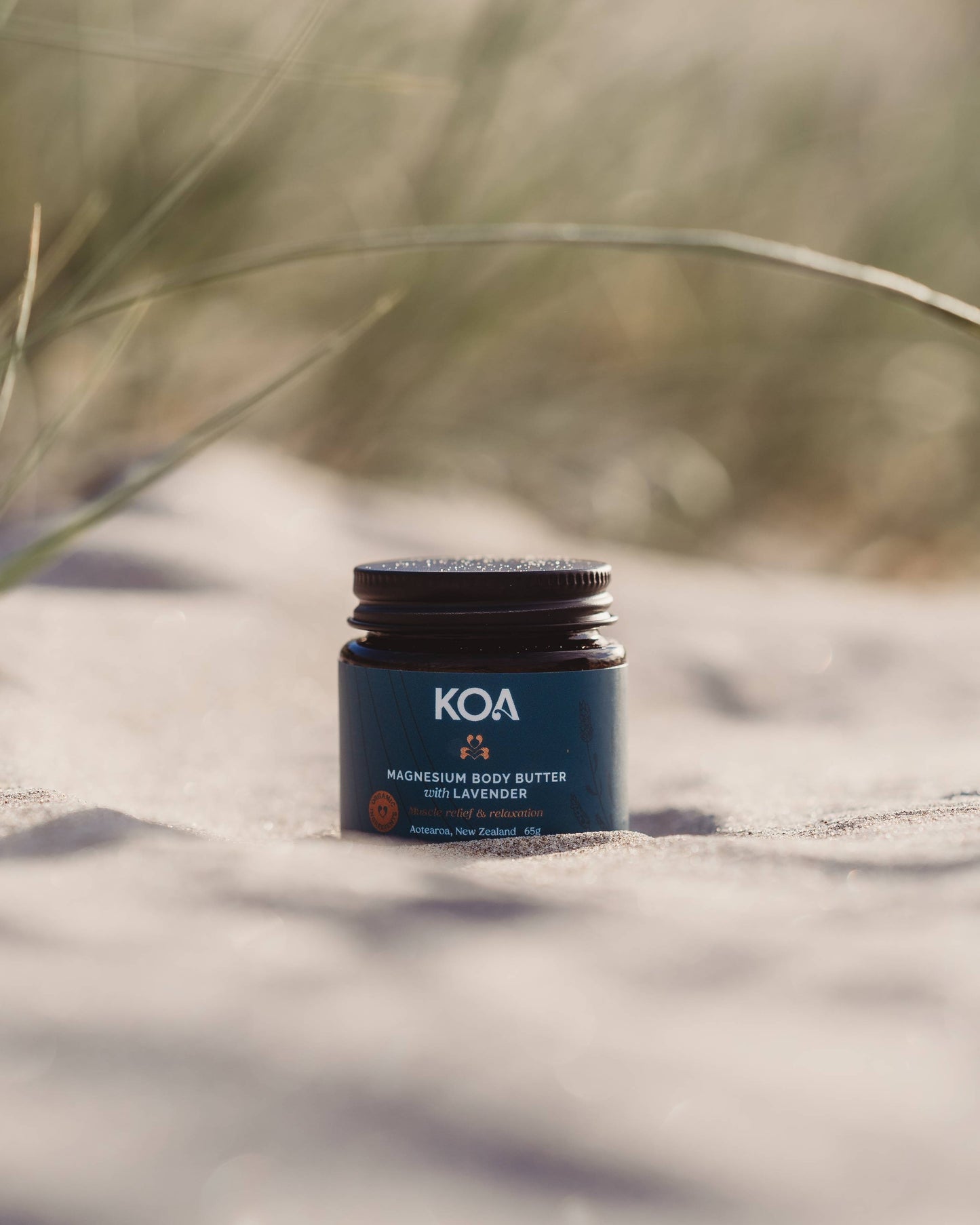 Magnesium Butter with Lavender sitting on the sand with grasses behind.