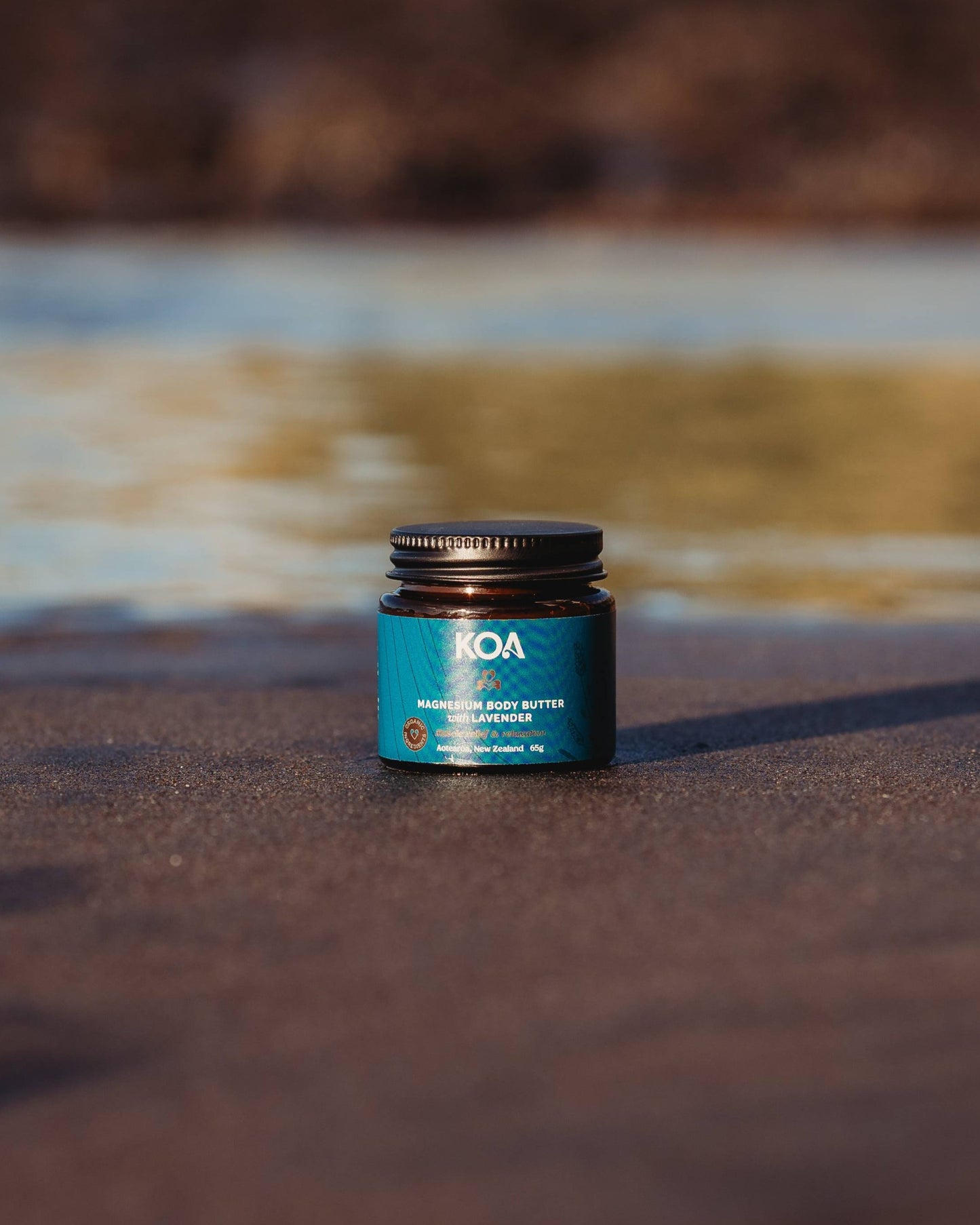 Magnesium Butter with Lavender sitting on the sand with an ocean background.