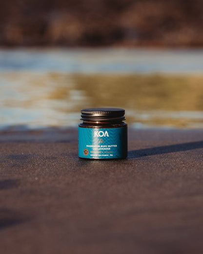 Magnesium Butter with Lavender sitting on the sand with an ocean background.