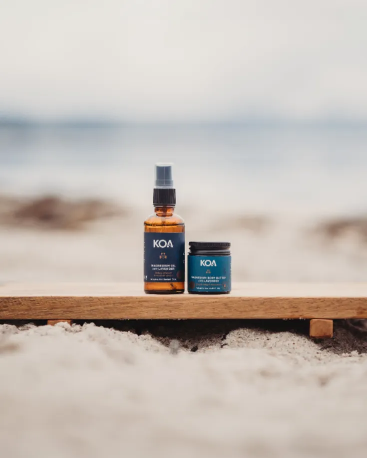 Magnesium Oil and Butter with Lavender sitting on a wooden plinth in the sand with ocean background.