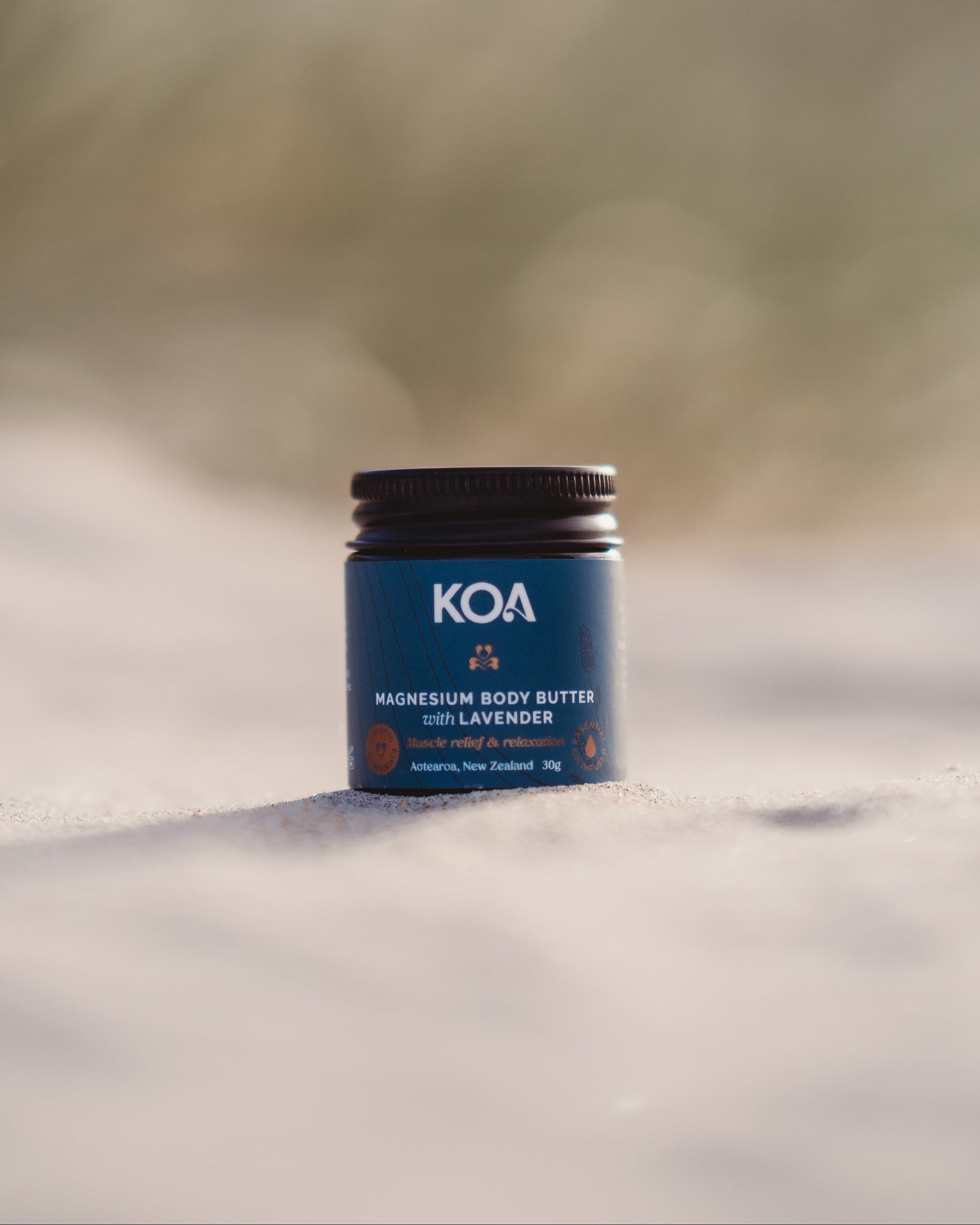 KOA magnesium body butter jar on a sandy surface with grasses in the background