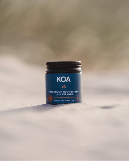 KOA magnesium body butter jar on a sandy surface with grasses in the background