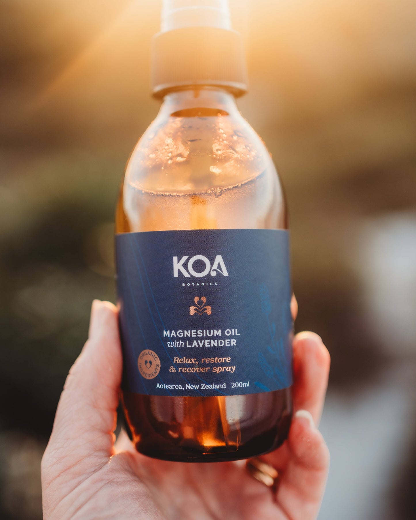 Close up of Magnesium Oil with Lavender being held in a hand with a scenic background.