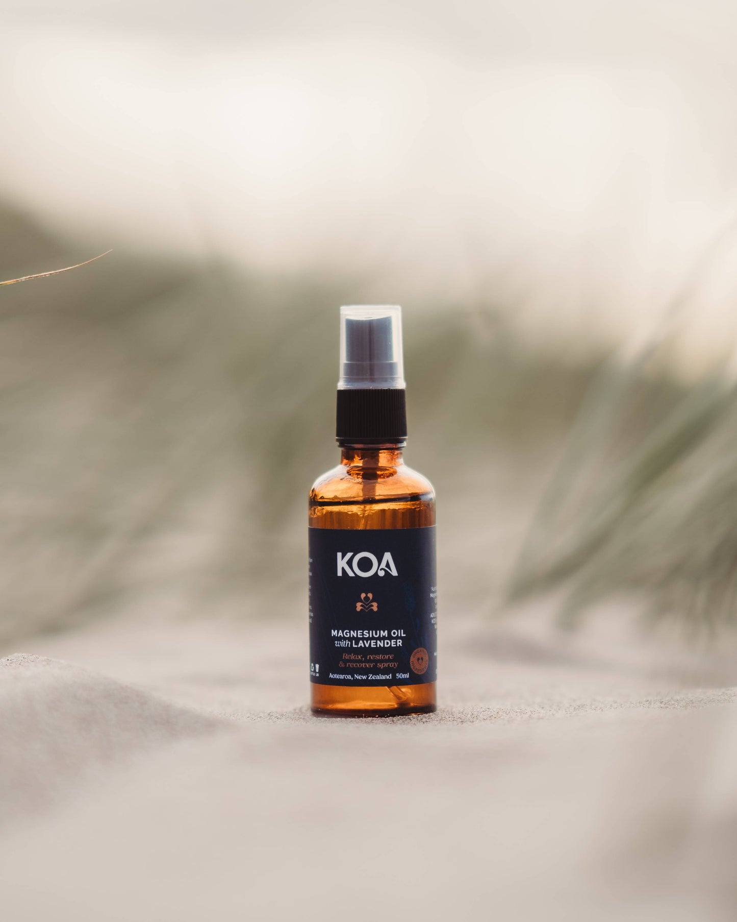 Magnesium Oil with Lavender sitting on the sand with grasses behind.