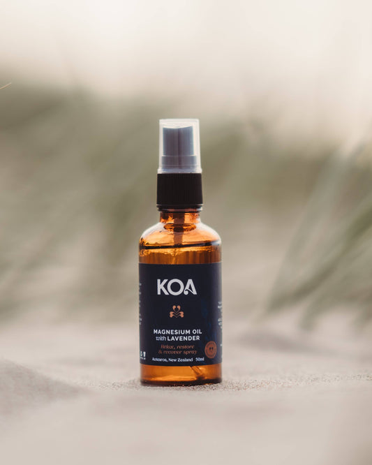 Magnesium Oil with Lavender sitting on the sand with grasses behind.