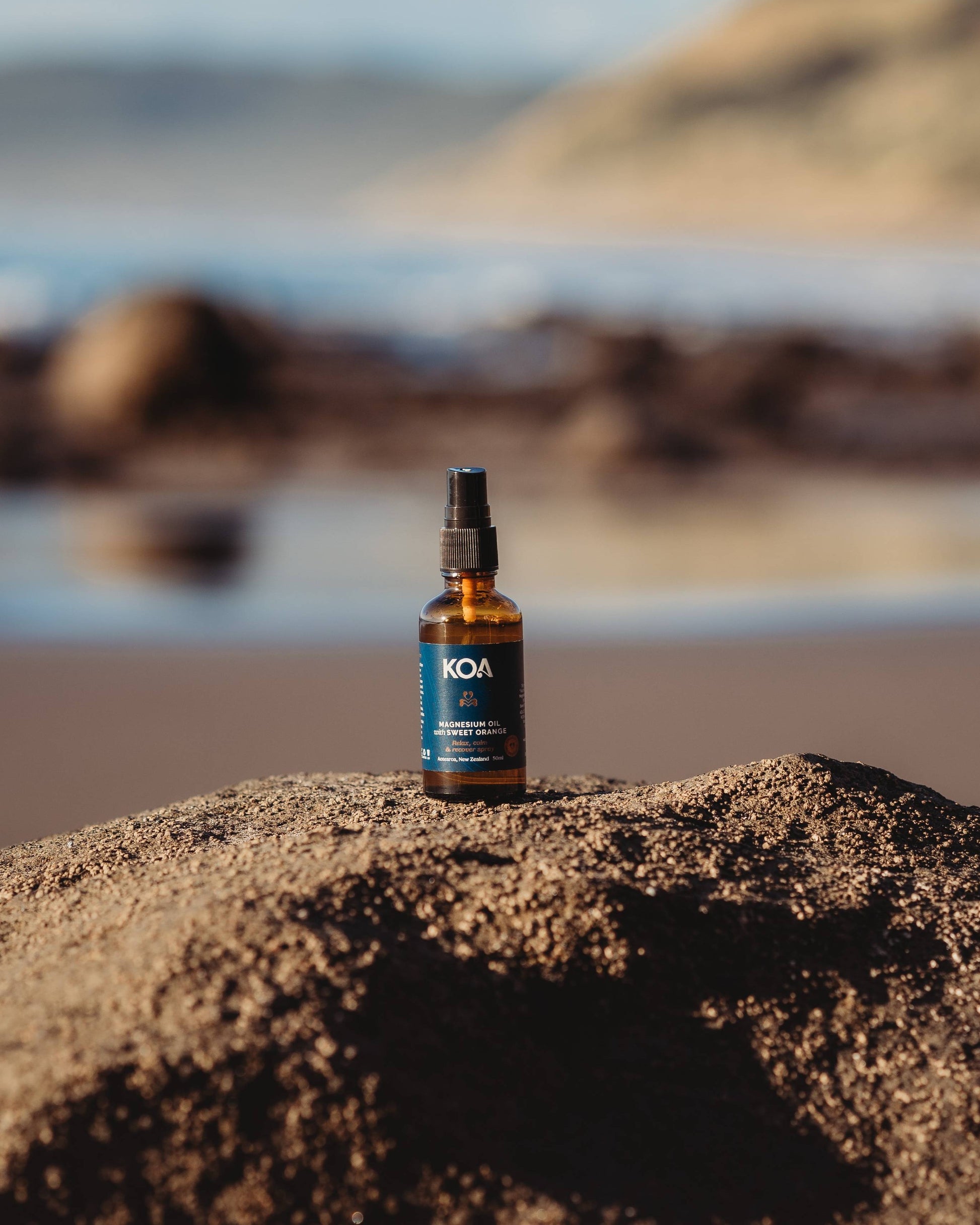 Magnesium Oil with Sweet Orange sitting on a rock with an ocean background.