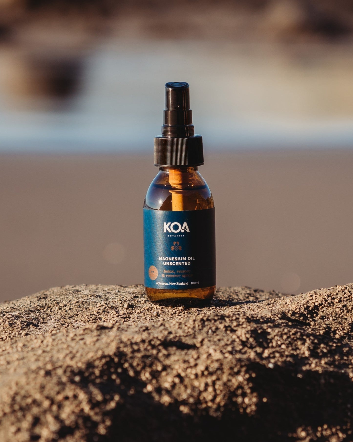 Magnesium Oil Unscented sitting on a rock with an ocean background.