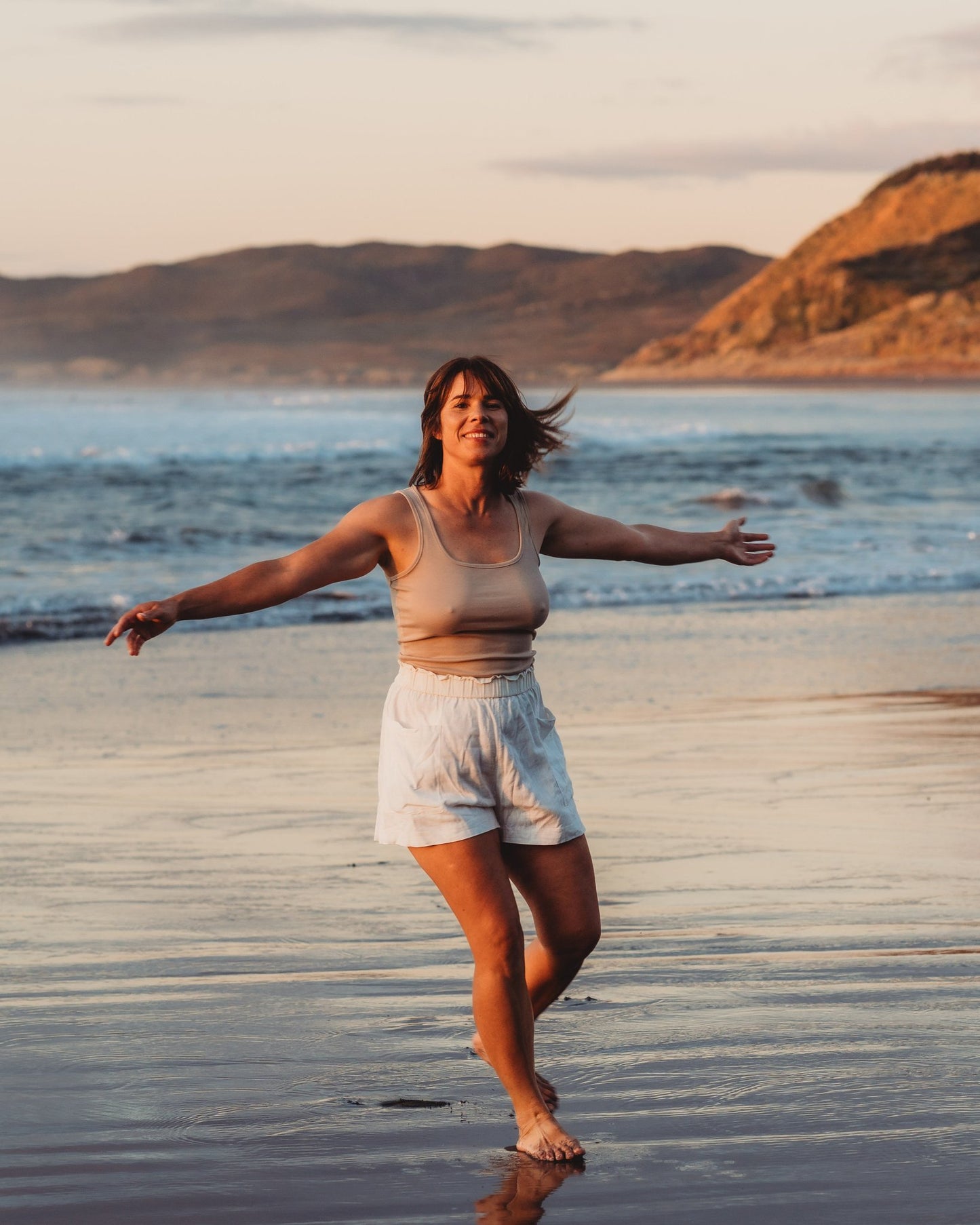 A full length lady looking happy on the beach with a scenic ocean background.